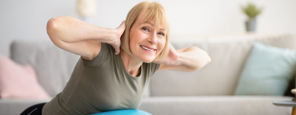 Smiling senior woman doing exercises with fitness ball at home, space for text